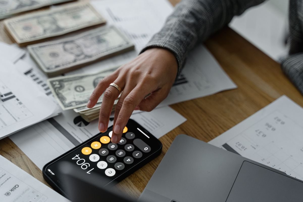 Una persona usa una calculadora para revisar dinero y documentos.
