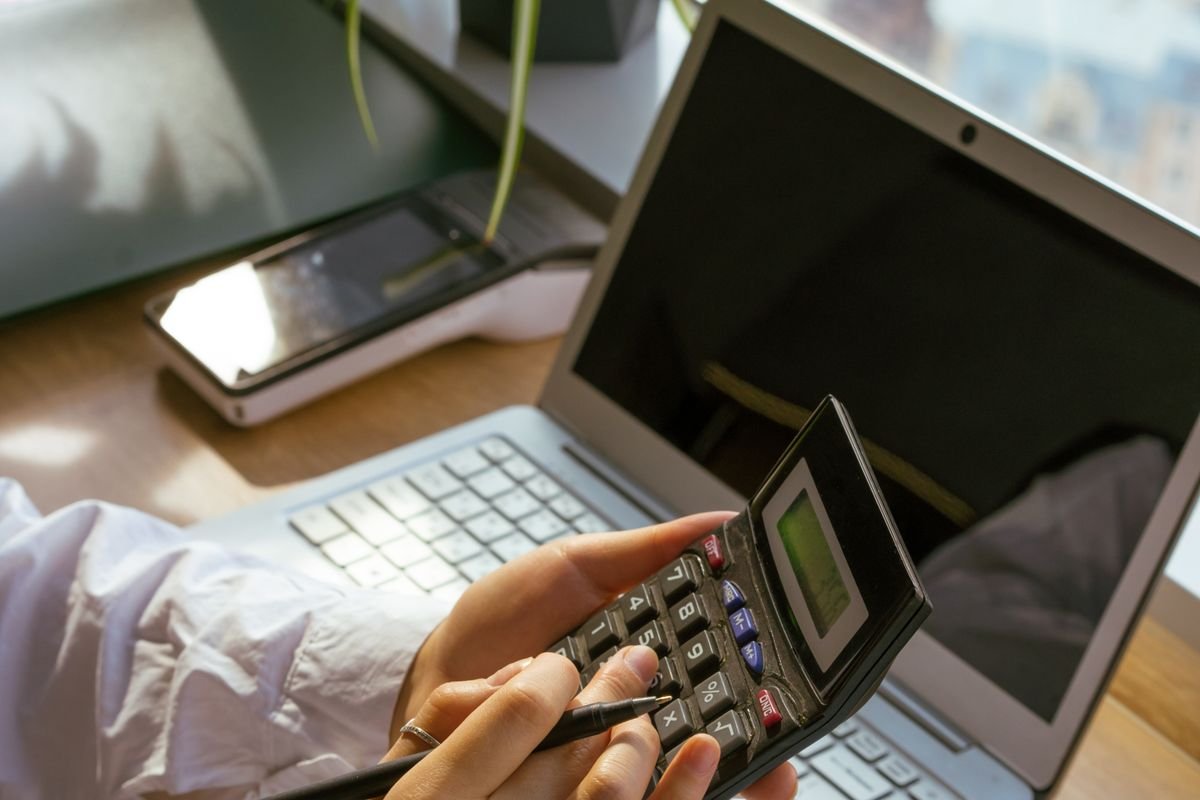 Una persona trabaja con una computadora y una calculadora en su escritorio.
